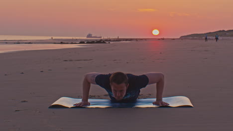 white slim caucasian european dutch man male model does sunset training sports exercises push-ups on the beach sand seashore in netherlands north sea with setting sun on the background