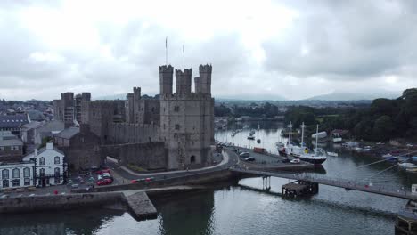 Ancient-Caernarfon-castle-Welsh-harbour-town-aerial-view-medieval-waterfront-landmark-reverse-reveal-skyline