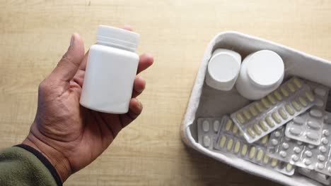 hand holding a white medicine bottle with other drug containers in a basket on a table