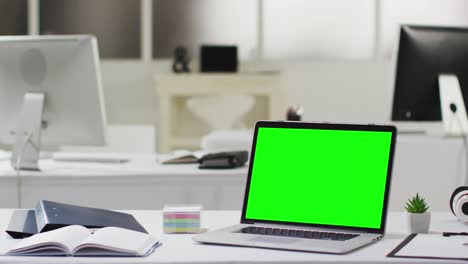 Laptop-with-green-screen-on-desk-in-empty-modern-office-space,-slow-motion