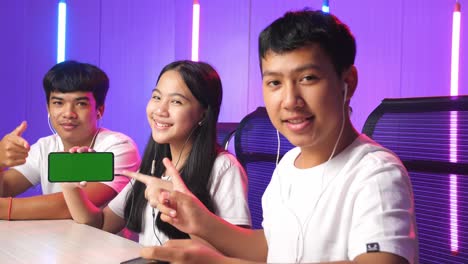team of asian gamers sitting on chair and pointing to mock up green screen mobile phone