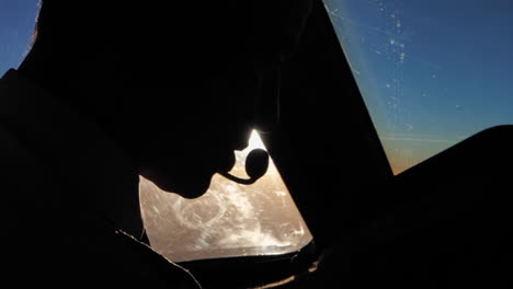 closeup silhouette of a male pilot in the cockpit talking over headset communication device while in flight at sunset