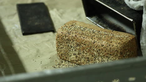 hands of a baker remove freshly baked loaf bread with sesame seeds from a baking pan