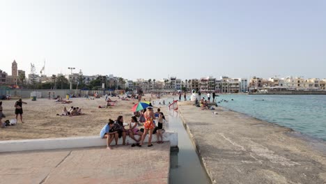 busy beach scene with people, pier, and coastal buildings