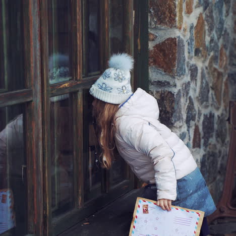 little girl is looking through the small wooden windows outdoors. curious child looks inside the house with fairy atmosphere while standing near the windows in winter.
