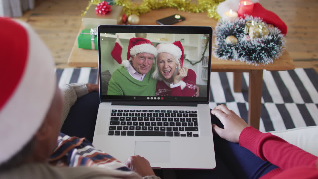 madre y hija afroamericanas usando una computadora portátil para una videollamada de navidad con la pareja en la pantalla