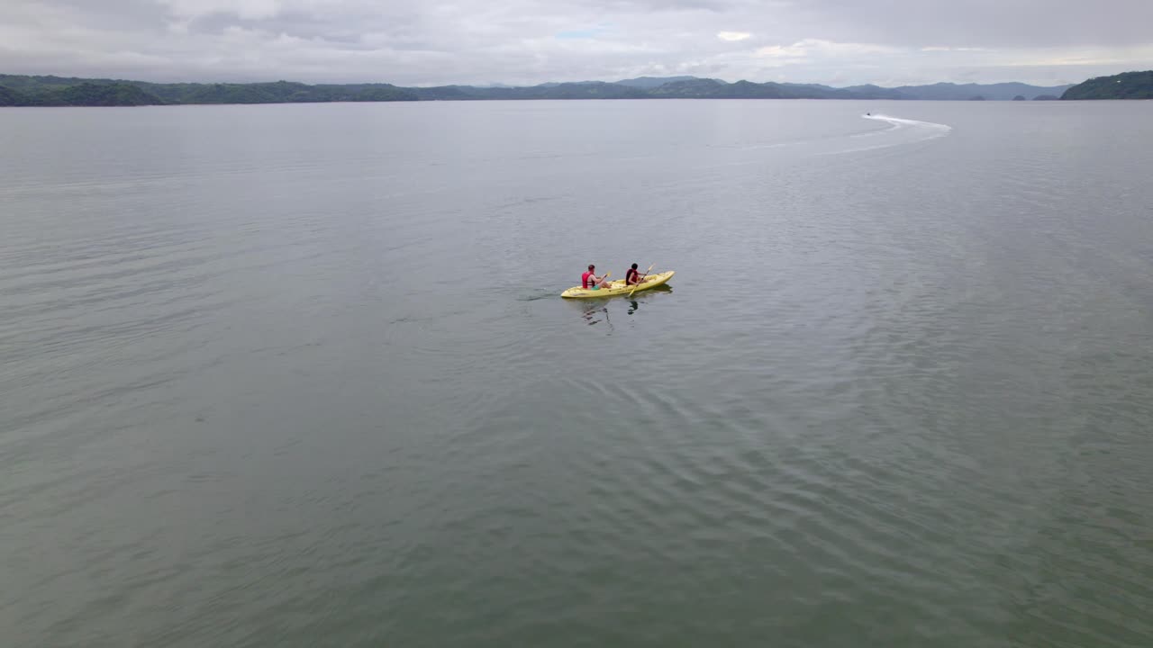 воздушная орбита людей, занимающихся каякингом в спокойном море рядом с причалом и холмами, покрытыми лесом, пляж накасколо, полуостров папагайо, коста-рика