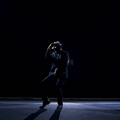 actor making funny dance on a stage. silhouette of a man in costume and hat dancing in dark background. amusing performance on scene