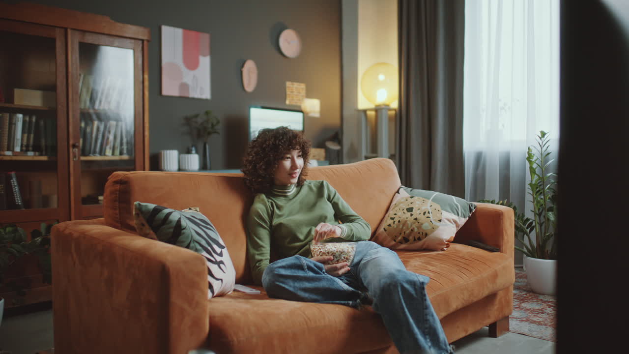 Young Asian Girl Eating Popcorn and Watching TV at Home