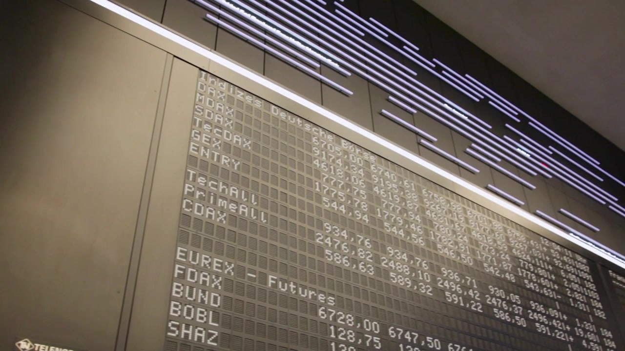 Un tabellone elettronico della borsa mostra numeri e indici in evoluzione in un interno moderno.