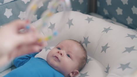 mother plays with small son shaking funny rattle above crib