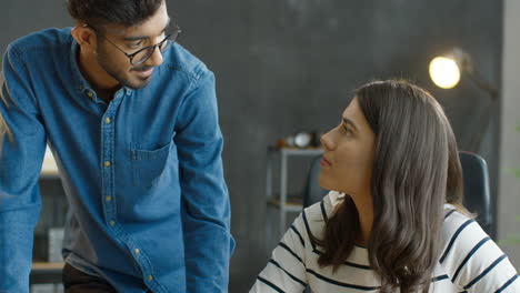 Hombre-árabe-Y-Mujer-Morena-Hablando-Y-Discutiendo-En-El-Escritorio-Frente-A-La-Computadora-Portátil-En-La-Oficina