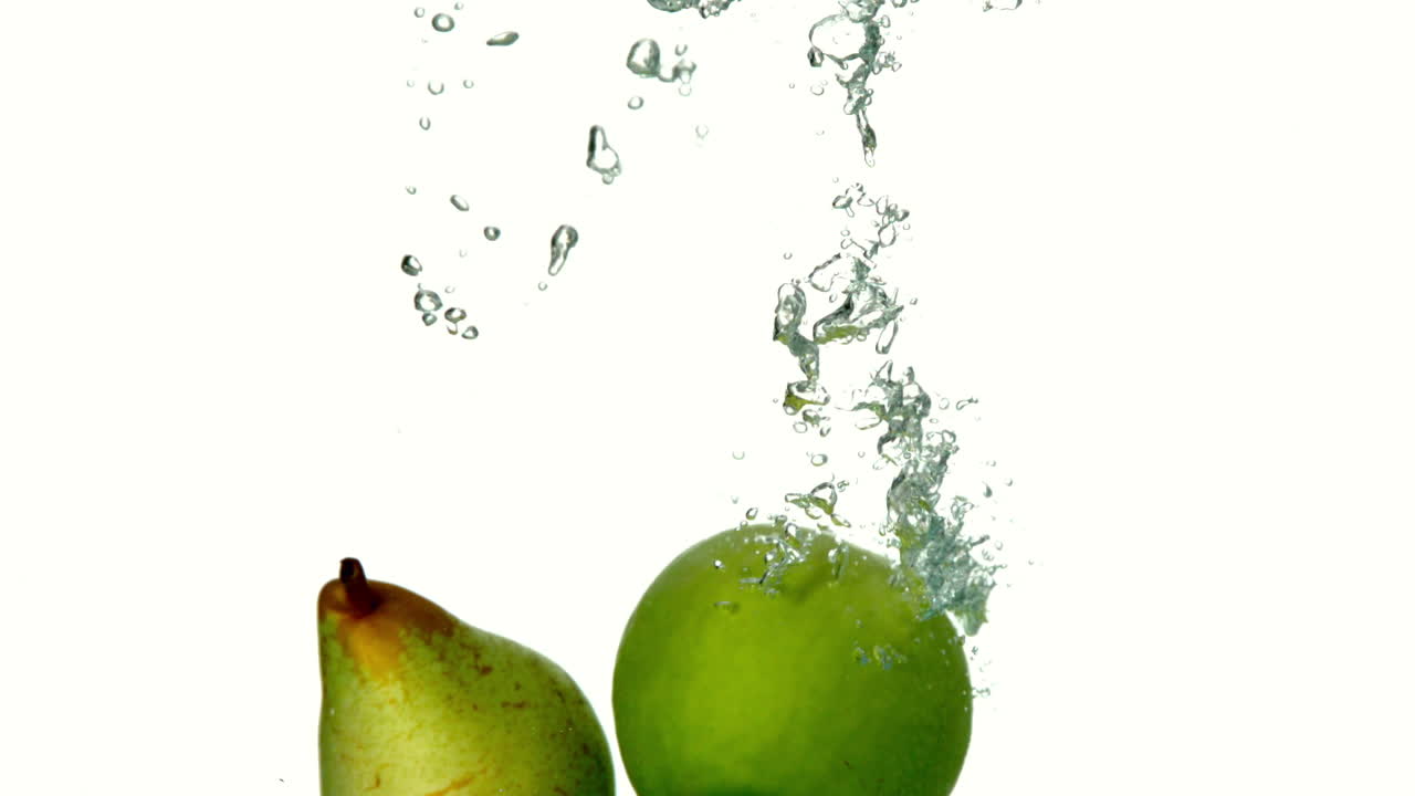 pera y manzana sumergiéndose en el agua sobre un fondo blanco