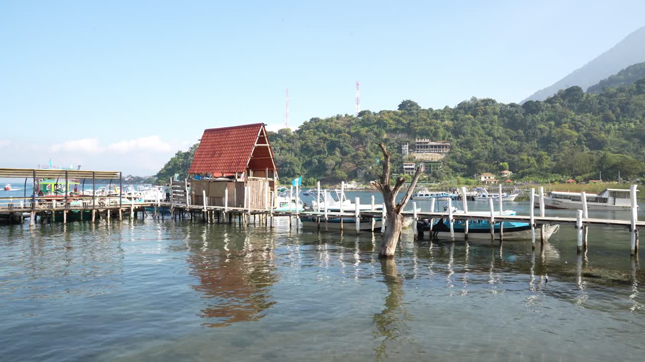 Wooden pier on the calm Lake Atitlan, with small boats anchored and a mountain with green vegetation in the background. Video shot on the shores of Panajachel.