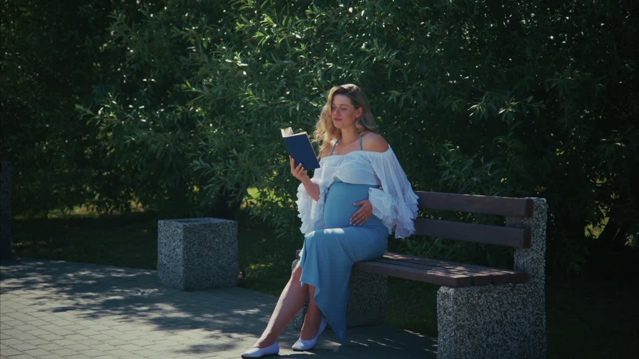 Glad gravid kvinde læser en bog på en parkbænk