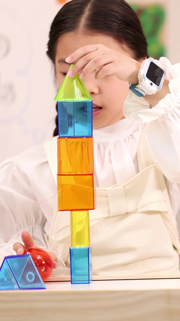 Giovane ragazza impila con cura blocchi magnetici colorati di geometria in un'aula luminosa, inquadratura ravvicinata statica