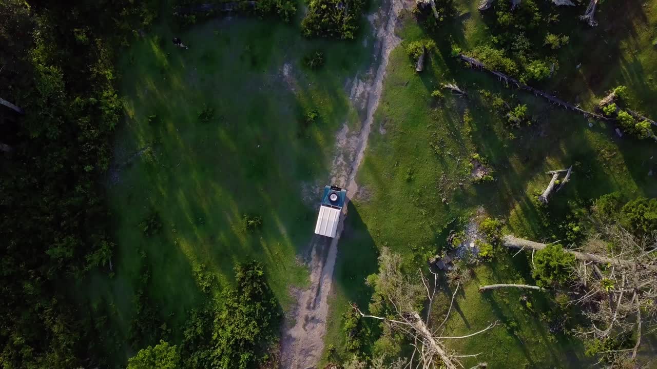 Aerial view above a off road truck driving on a forest dirt road, in rough terrain, at Cerro El Volcan, El Hatillo, Venezuela - overhead, drone shot