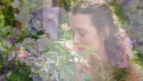 Animation-of-glowing-lights-over-happy-biracial-woman-smelling-flowers-in-garden