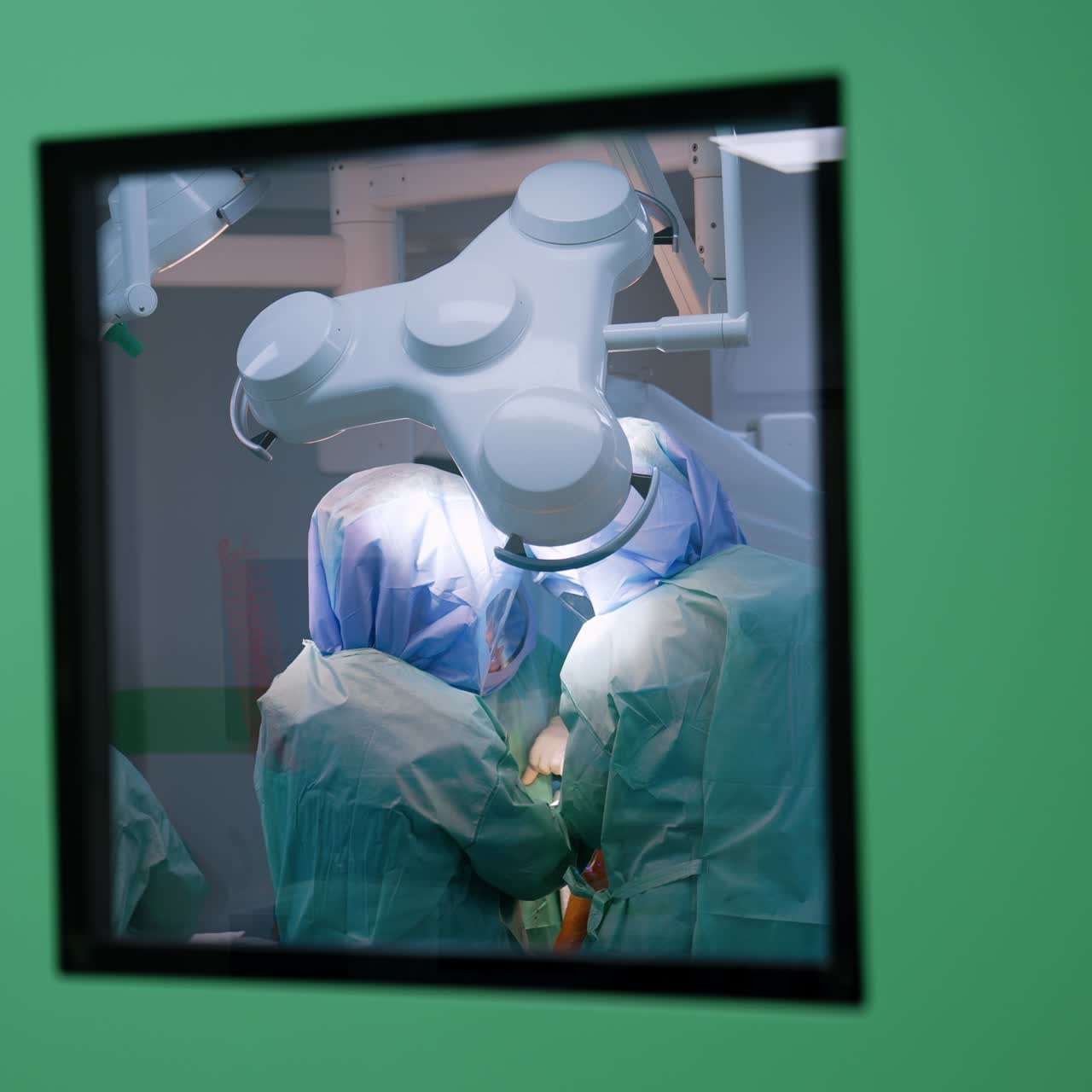 Footage at the window in the surgery room door. Medical team wearing protective suits works at operation