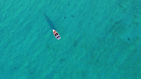 la luz del sol brilla en las claras ondas de agua turquesa mientras un barco de pesca anclado en la arena flota en el océano.