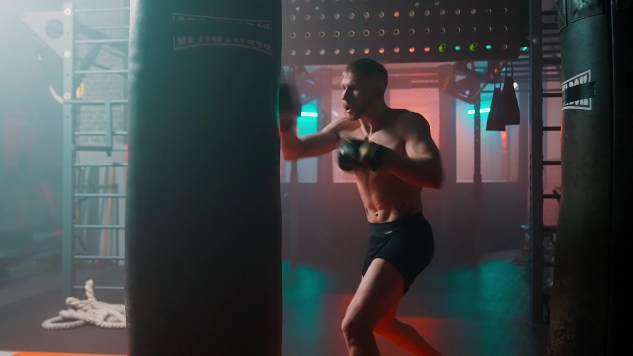 Boxeador Masculino Sem Camisa Treinando com Saco de Pancadas em uma Academia Escura