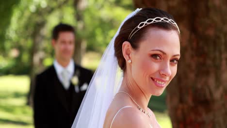 Bride-smiling-at-camera-with-groom-standing-in-background