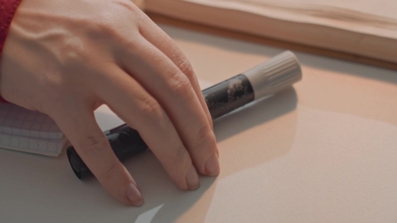 Hand interacts with worn pen on graph paper notebooks. Scene includes open book and consistent lighting. Cylindrical object is grasped moved slightly then displaced by same left