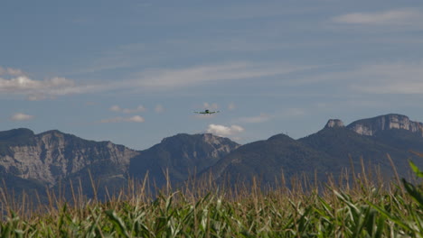 airplane flying over cornfield and mountains