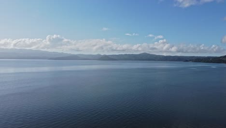 Aerial-top-view-of-peaceful-calm-dark-blue-sea-water-surface,-cloudy-sunset-or-sunrise-sky-and-silhouettes-of-mountains