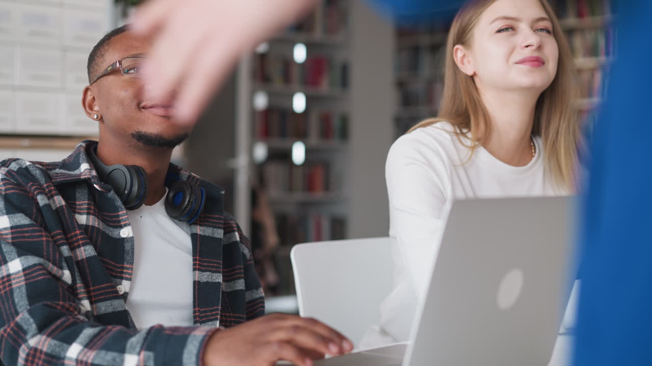 estudiantes felices escuchan a la maestra en la biblioteca pública. mujer sonriente y chico negro con portátil miran al mentor en la sala de lectura de la universidad. lección moderna