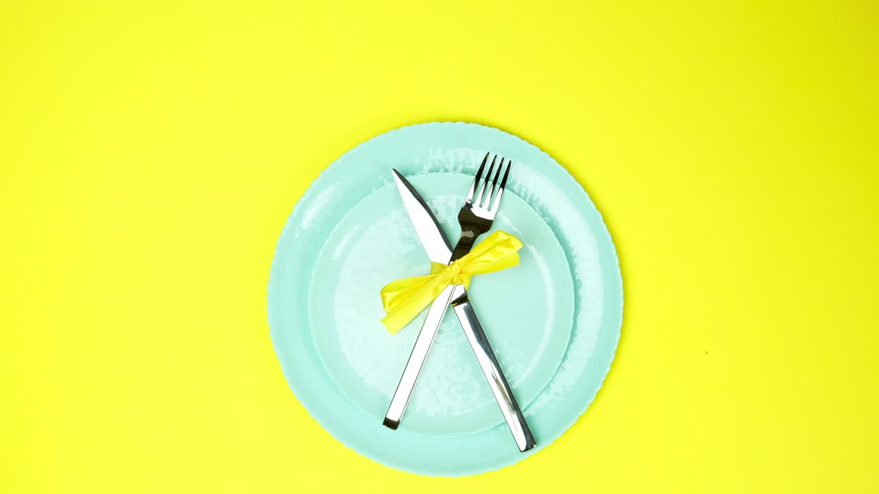 two female hands put metal knife and fork tied with yellow ribbon on empty plates, top view, yellow background,