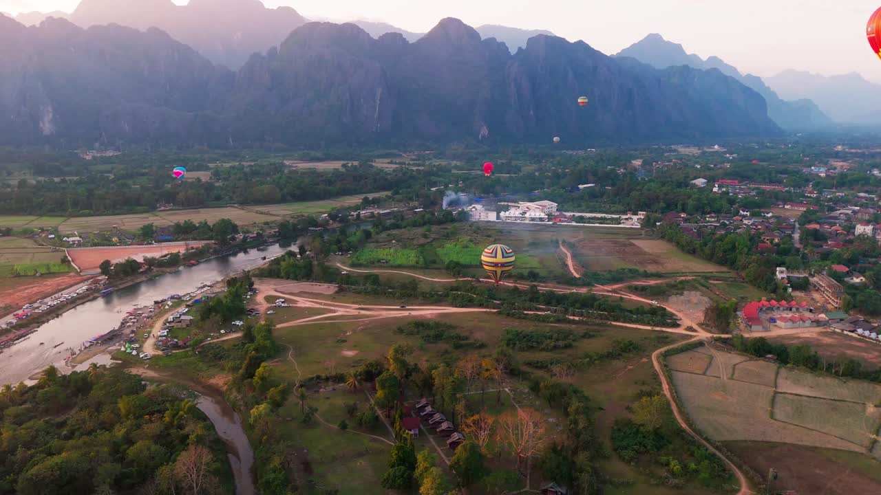 Hot air ballons fly above Vang Vieng town in Laos, Aerial view of touristic leisure area around tropical mountains
