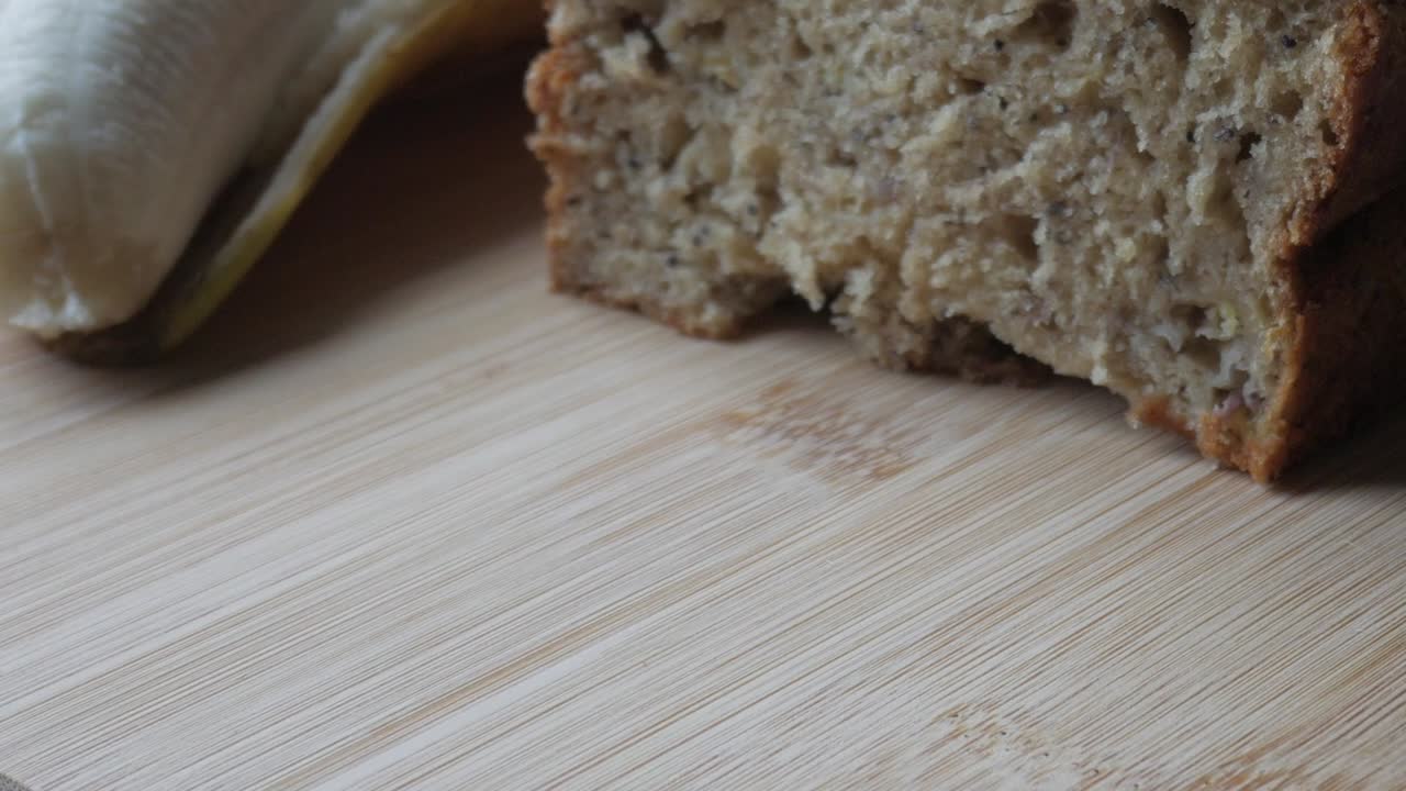 Freshly baked banana bread sits on a wooden cutting board with soft texture and crumbs visible