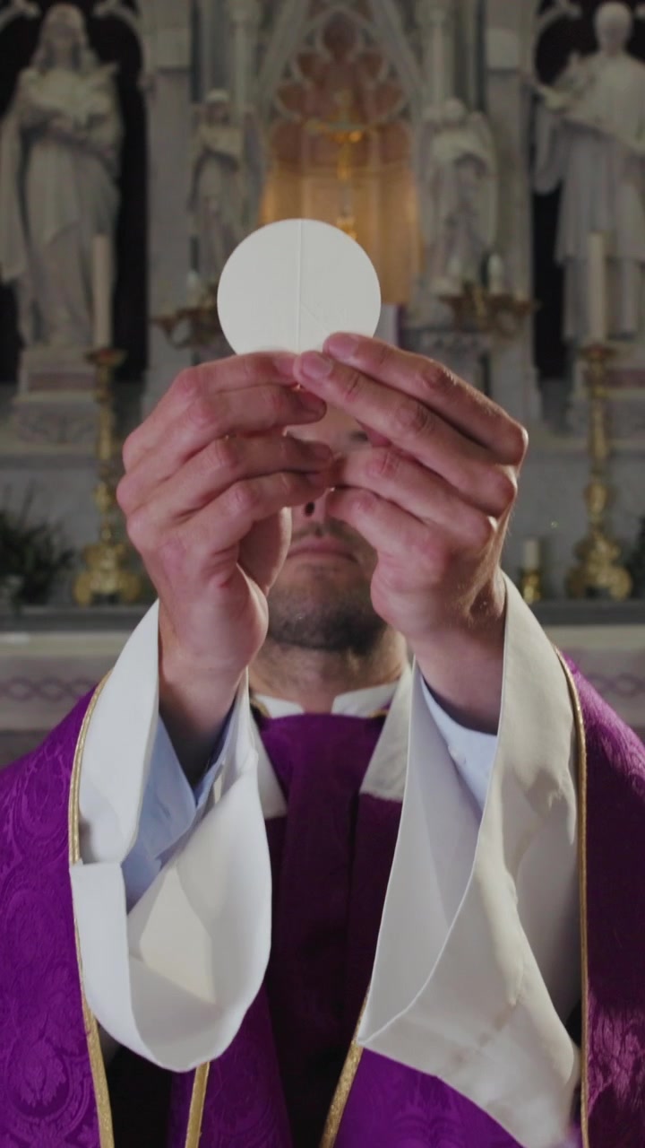 Kněz sloužící katolickou mši pozvedá eucharistickou hostii z pateny umístěné na oltáři.