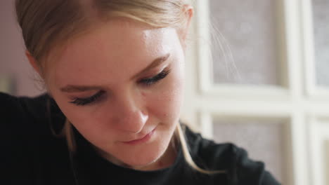light skin blonde woman with hair parted at middle and tucked behind ear, looking down and smiling softly with full eyelashes, against softly blurred background and frosted glass panels