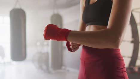 Video-De-La-Sección-Media-De-Una-Mujer-Caucásica-Atando-Cintas,-Preparándose-Para-El-Entrenamiento-De-Caja-En-El-Gimnasio