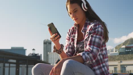 Smiling-caucasian-woman-wearing-headphones-and-using-smartphone-at-a-skatepark