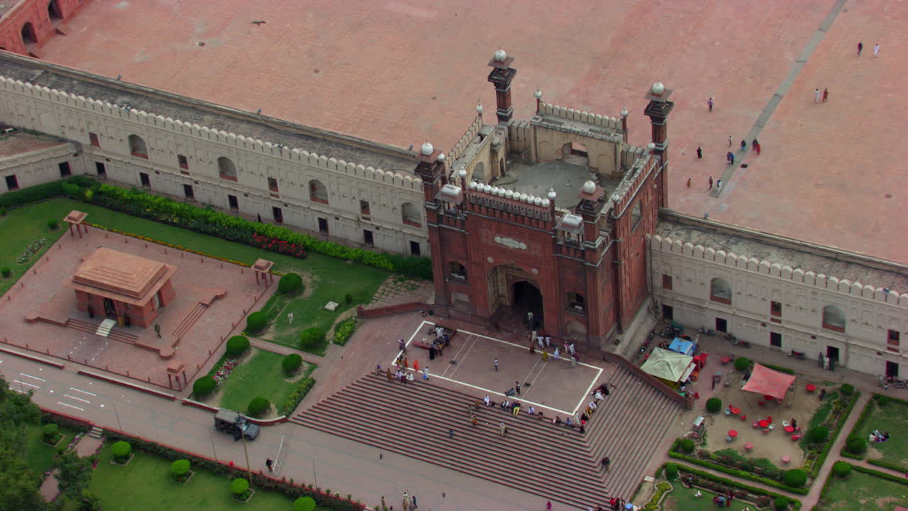 lahore, pakistán, zoomando en la vista aérea de la entrada de la mezquita badshahi, visitantes damas, caballeros y niños sentados en las escaleras de la mezquita, la gente entrando en la mezquita