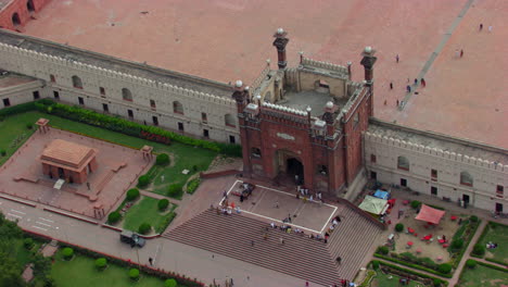 lahore, pakistan, zooming in aerial view of the entrance of the badshahi mosque, visitors ladies, gents and children sat the stairs of the mosque, people entering in the mosque