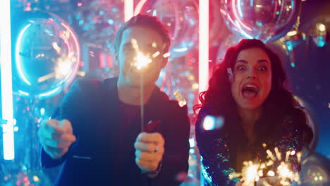 Happy-man-and-woman-holding-sparkles-in-club.-Couple-dancing-with-bengal-lights