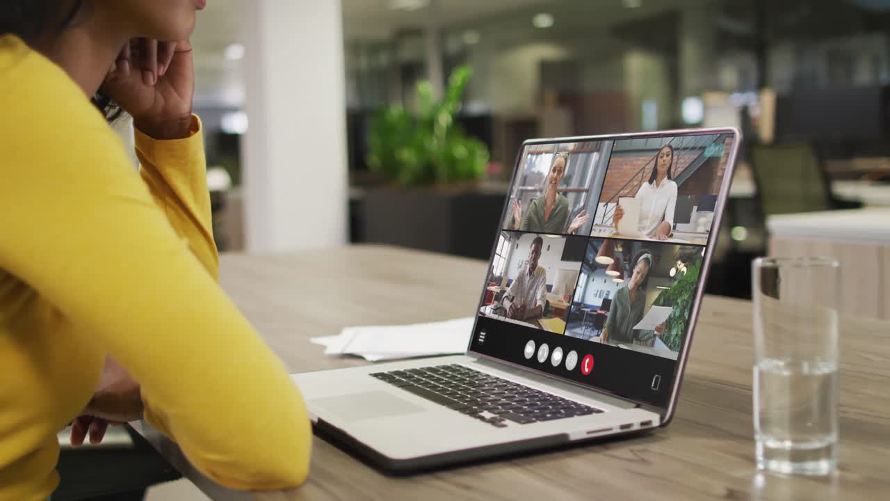 Biracial woman using laptop for video call, with diverse business colleagues on screen