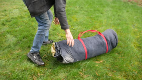 a man taking a tent out of a bag, unpacking it and laying it on the grass