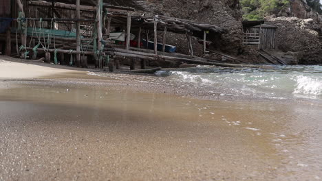 Zeitlupe-Von-Wellen,-Die-An-Einem-Tropischen-Strand-Mit-Altem-Holzbootshaus-Im-Hintergrund-Zusammenbrechen