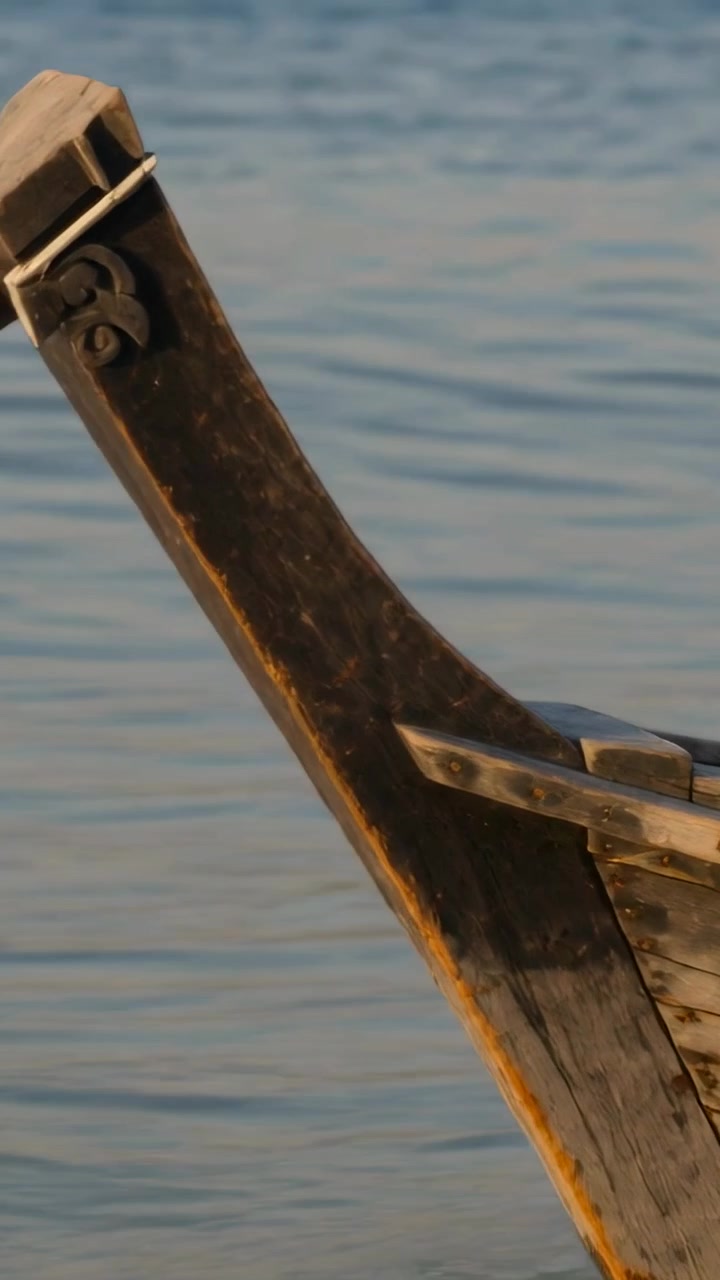 Video verticale: Telecamera che si inclina rivelando la prua di una barca sulla destra sul mare, mostrando un elemento intagliato, con spazio per il testo.