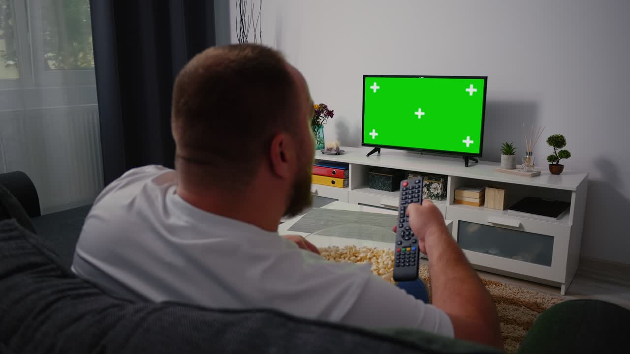 Mand ser tv-skærm med grøn Chroma Key og skifter kanal med fjernbetjeningen flere gange