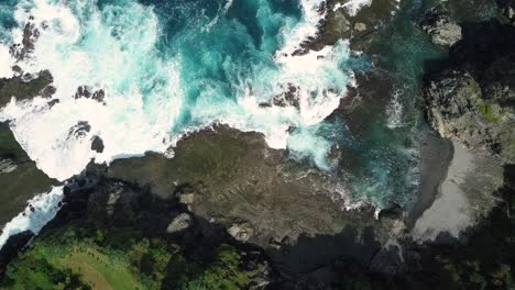 aerial top down of massive waves crashing against rocky coastline and beach