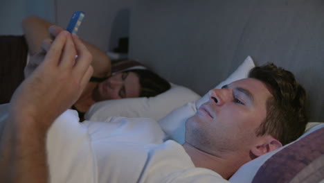 man using mobile phone in bed whilst partner sleeps