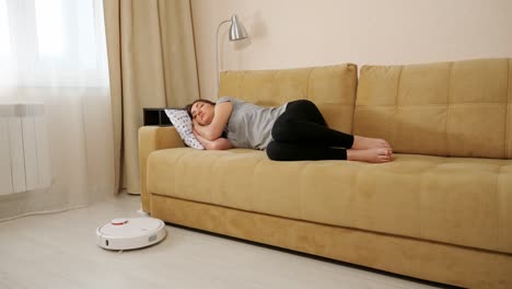 lady sleeps on sofa while robot cleaner hoovers in room