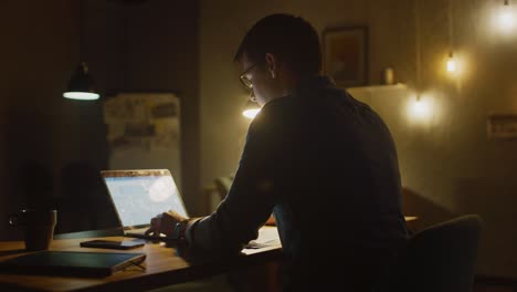 professional man sitting at his desk in office studio working on a laptop in the evening. man working with data, analyzing statistics, writing down information. 360 degree tracking arc shot movement