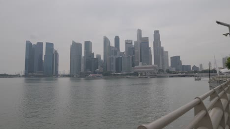 Wide-shot:-Camera-pans-across-the-impressive-architecture-of-the-Singapore-skyline-on-a-gray-day,-with-water-in-the-foreground